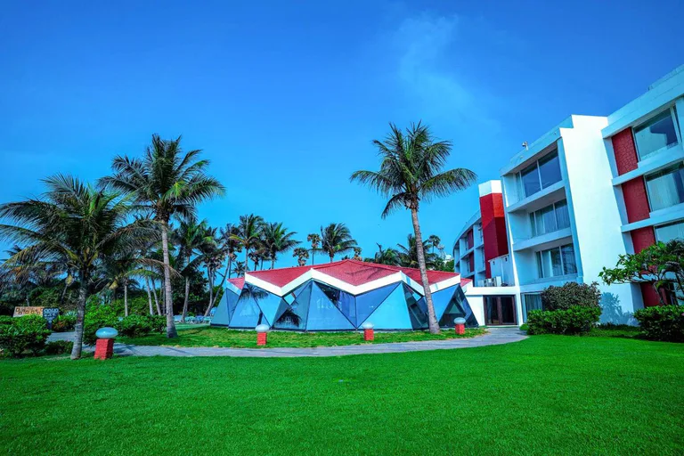 The Park Visakhapatnam hotel exterior with modern architecture, lush green lawn, palm trees, and clear blue sky.